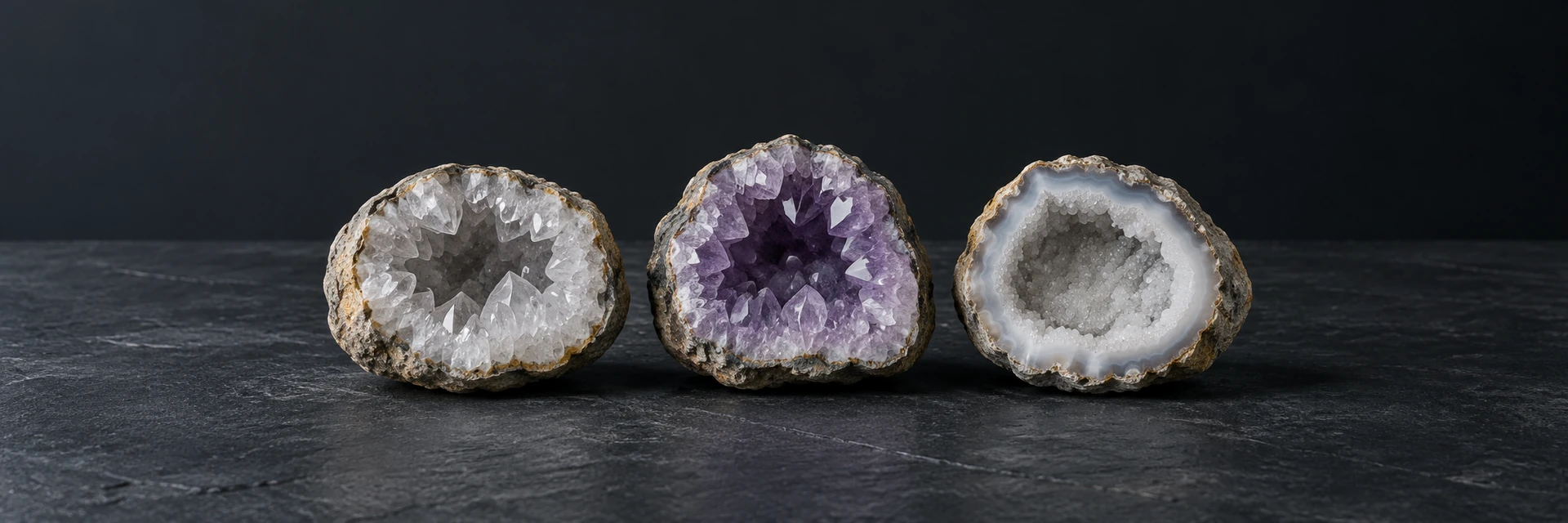 Opened quartz, amethyst and druzy quartz geodes with rough rinds on dark slate.