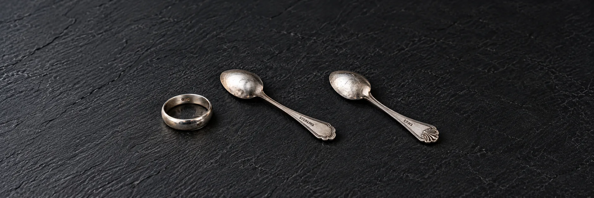 A silver-colored ring marked 925 and two complete spoons marked STERLING and EPNS on dark slate.